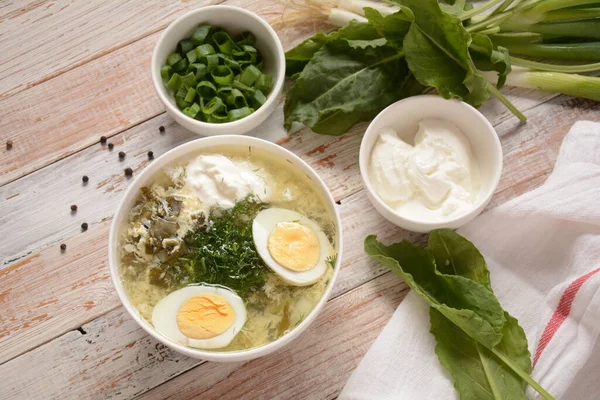 Green sorrel and spinach soup with boiled egg, spring onion and sour cream on white wooden rustic table. Diet or healthy food concept — Stock Image Green Sorrel Spinach Soup Boiled Egg Spring Onion Sour Cream Stock Photo