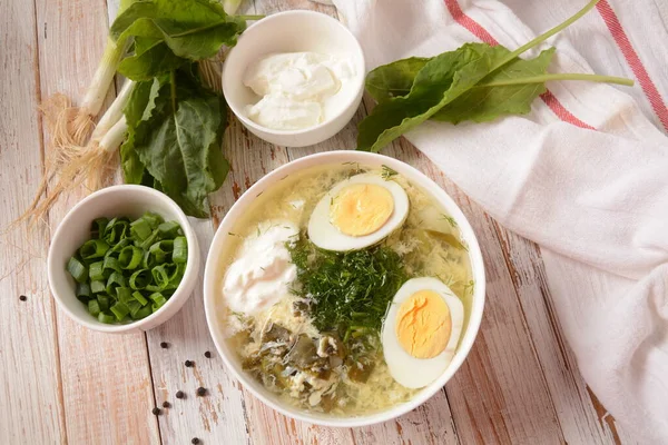 Green sorrel and spinach soup with boiled egg, spring onion and sour cream on white wooden rustic table. Diet or healthy food concept — Stock Image Green Sorrel Spinach Soup Boiled Egg Spring Onion Sour Cream Stock Photo