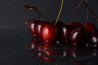 Siyah zemin üzerinde yansıması olan bir damla su olan kirazlar.