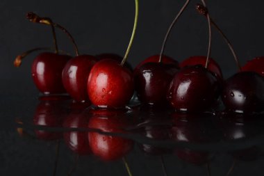 Siyah zemin üzerinde yansıması olan bir damla su olan kirazlar.