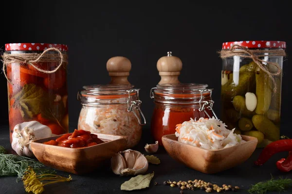 Jars of Homemade pickled vegetables: cucumbers, tomatoes, cabbage, on black background. Marinated and Fermented food. Fermented preserved vegetarian food concept.