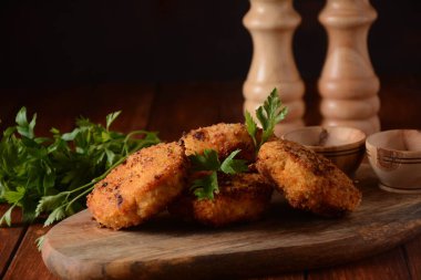 Sulu ev yapımı tavuk pirzolası. Ekmek kırıntılarıyla kaplı, lezzetli, eski siyah ahşap tahta üzerinde, kırsal tarzda, baharatlar ve otlarla kaplı.. 