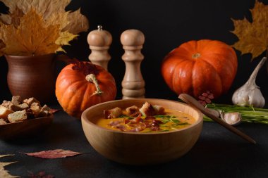 Kremalı balkabağı ve pastırmalı tatlı patates çorbası (batata). Bir kase ev yapımı kızarmış ekmek ve sonbahar dekorasyonlu otlar..