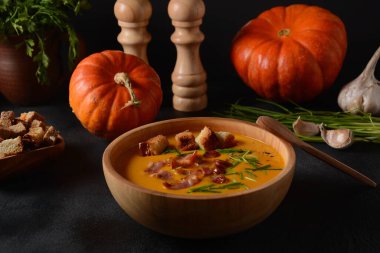 Kremalı balkabağı ve pastırmalı tatlı patates çorbası (batata). Bir kase ev yapımı kızarmış ekmek ve sonbahar dekorasyonlu otlar..