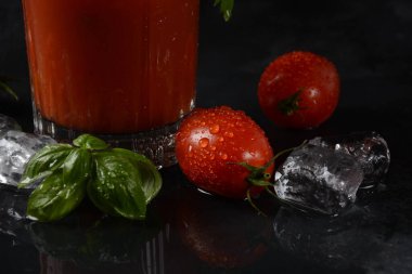 Bir bardak taze domates suyu ve domatesler koyu arka planda su damlalarıyla