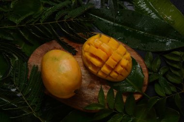 Dilimlenmiş mango parçalı taze mango meyvesi tabakta ya da yapraklarda arka plan olarak. 