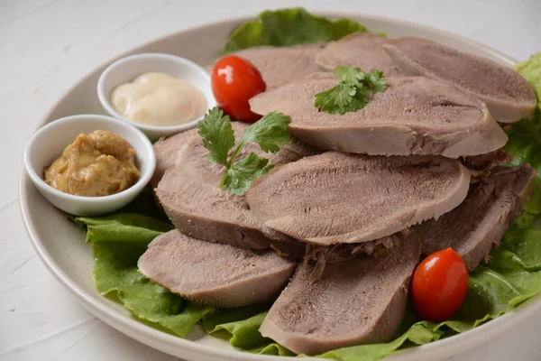 Dilimlenmiş Biftek Dili Marul yaprakları, kiraz domatesleri ve ahşap bir arka planda Dijon hardalı ile bir tabakta dilimler.