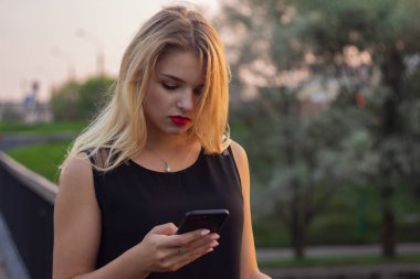 Sarışın genç kız parkta cep telefonu kullanarak, halka açık yerlerde wifi ile modern gadget. Freelancer kız parkta çalışan ve arkadaşları ile sohbet