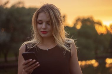 Sarışın genç kız parkta cep telefonu kullanarak, halka açık yerlerde wifi ile modern gadget. Freelancer kız parkta çalışan ve arkadaşları ile sohbet