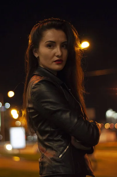 Street style, mode. Portrait d'une femme en noir avec un beau maquillage et rouge à lèvres sur la route avec rétro-éclairage, lumières vives et la lumière des lanternes — Photo