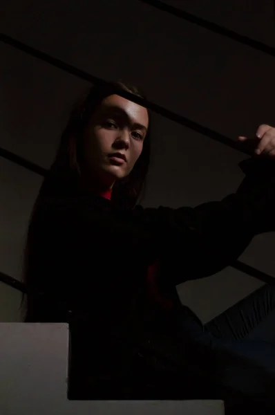 Junge schöne stilvolle Frau in schwarzem Sakko und hessischen Stiefeln, die auf einer Treppe im modernen Interieur sitzt. Mode-Stil Porträt mit hartem Licht — Stockfoto