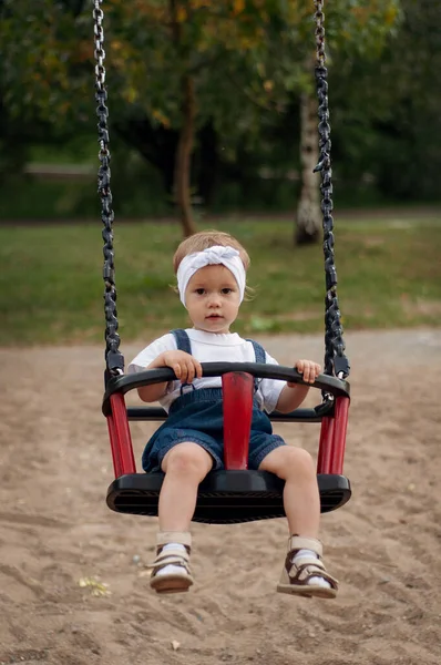 A little girl swinging on a red children swing — Stock Photo, Image