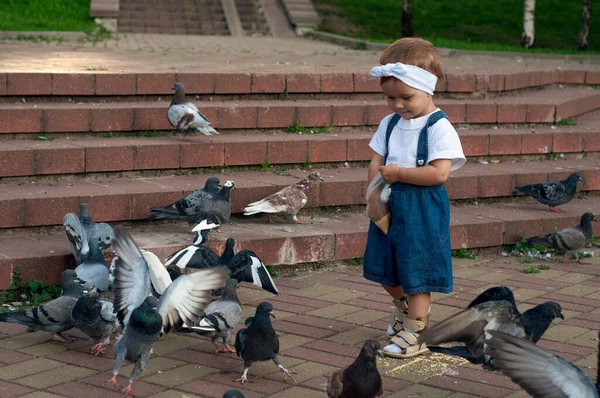 Niña corriendo cerca de palomas, persiguiendo palomas, niña feliz con la cara sonriente. El chico está alimentando palomas en el parque de la ciudad. — Foto de Stock