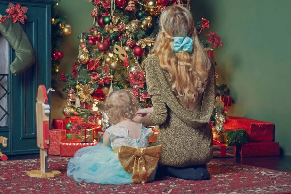 Mãe com uma pequena filha senta-se no tapete no apartamento no fundo da decoração de Ano Novo — Fotografia de Stock