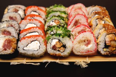 Büyük suşi seti farklı maki ile - hosomaki, futomaki ve uramaki üzerine siyah arkaplanda eşleşir..