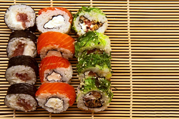 set of sushi roll on a bamboo plate or mat on a black background. three types of sushi of different colors and types, Futomaki, Uramaki and Hosomaki