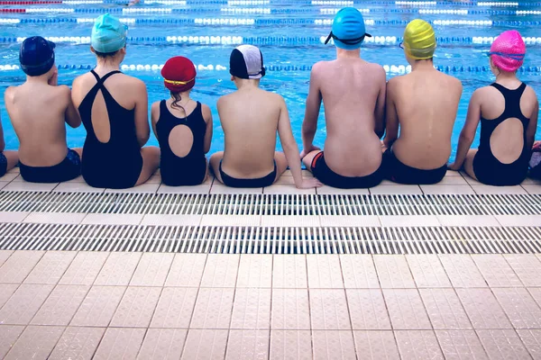 一群穿着泳衣坐在游泳池旁的快乐的小孩的背影 — 图库照片