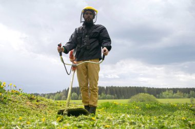 Bahçıvan bir el çim biçme makinesi ile sarı karahindiba biçer. Eller budayıcı, seçici odaklanma