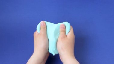 Çamurla oynamak, eğlence ve stres atmak için yapışkan maddeyi germek. Yaklaş ve üst görünümde kadın eli mavi parlak balçık tutuyor, sıkıyor..