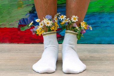 Çoraplarında taze çiçekler olan kadın bacakları. Renkli arka planda beyaz çorap çiçekleri olan genç bir hippi kız.