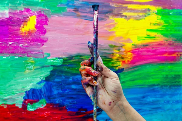 Close up of an artist or painter hands holding dirty paint brushes on colorful background picture