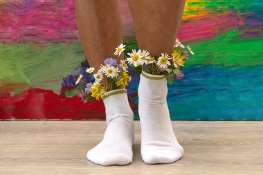 Çoraplarında taze çiçekler olan kadın bacakları. Renkli arka planda beyaz çorap çiçekleri olan genç bir hippi kız.