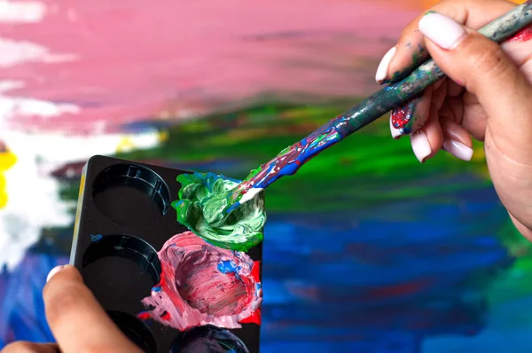 artist paints a picture of oil paint brush in hand with palette close up. Mixing gouache paint on a palette, creative