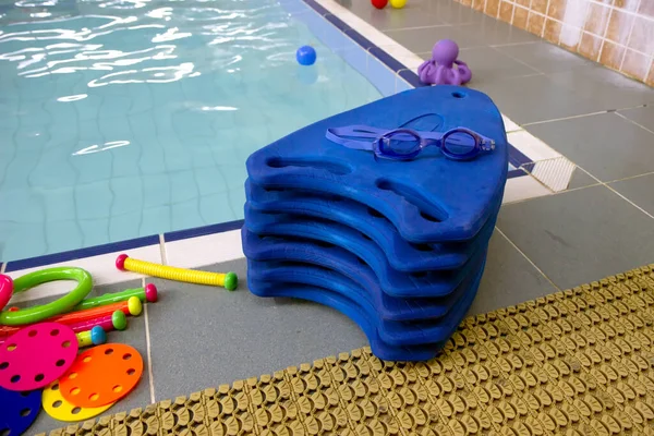 Blue swimming boards with swimming glasses and toys on beside of the pool