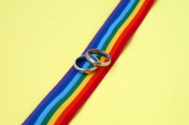 LGBTQ gökkuşağı kurdelesinde sarı arka planda bir çift altın alyans.