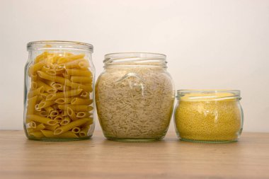 Tahta masadaki cam kavanozlarda pişmemiş mısır gevreği ve makarna çeşitleri. Sağlıklı yemek, temiz yemek, sıfır atık konsepti. Dengeli diyet yemekleri.