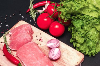 Çiğ, sulu biftekler siyah tebeşir tahtasında kızartılmaya hazır. Kiraz domatesli fileto, acı biber, bitkiler, biberiye, sarımsak.