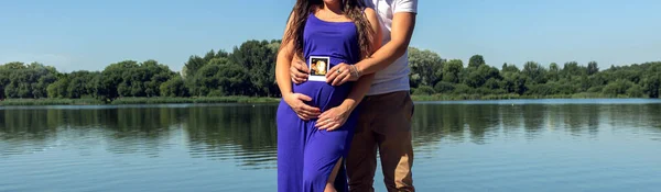 parents-to-be couple pregnancy holding ultrasound picture of future baby boy in the arms of her husband. banner