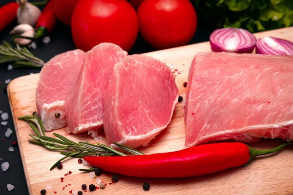 Bifes de carne suculentos crus prontos para assar em um fundo de placa de giz preto. filé com tomate cereja, pimenta e ervas. — Fotografia de Stock