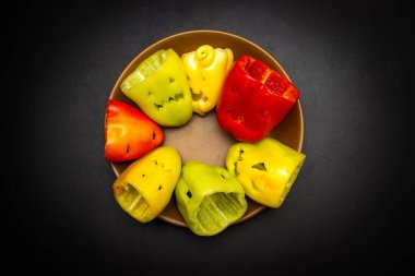 Çok renkli cadılar bayramı biberleri. Siyah bir arka planda, tabakta farklı yüzler var. Cadılar Bayramı hazırlığı, yemek ve abur cubur hazırlığı