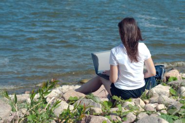 Kumsalda dizüstü bilgisayar kullanan genç bir kadın. Serbest çalışma konsepti, serbest yazar ve blogcu dışarıda. Boşluğu kopyala