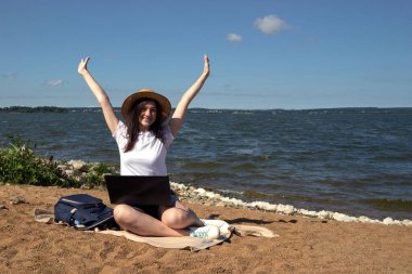 Genç bir kadın kumsalda güneşlenirken dizüstü bilgisayar kullanıyor. Serbest çalışma kavramı, serbest yazar ve blogcu dışarıda