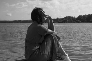 Rıhtımda nehir kenarında oturan üzgün kadın. içe dönük, yorgunluk ve depresyon kavramı