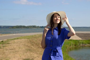 İskelede saman şapkalı, zarif elbiseli genç bir kadın harika bir manzaranın tadını çıkarıyor..