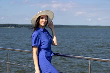 İskelede saman şapkalı, zarif elbiseli genç bir kadın harika bir manzaranın tadını çıkarıyor..