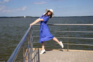 İskelede saman şapkalı, zarif elbiseli genç bir kadın harika bir manzaranın tadını çıkarıyor..