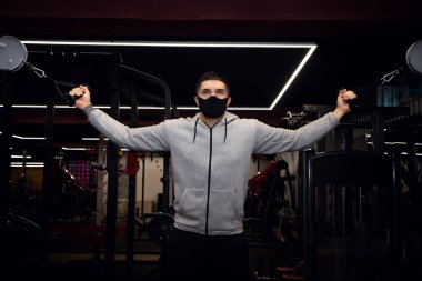 Spor salonunda göğüs ve kablo çaprazlama egzersizleri yapan kaslı bir adam. Tıbbi maskeli sporcu