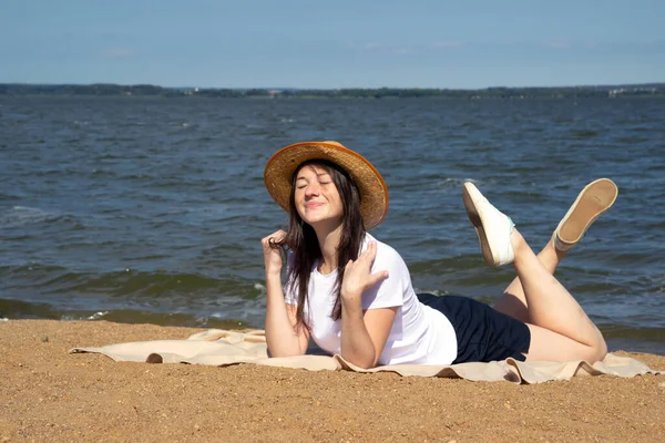 Temiz hava soluyan rahat bir kadının yan görüntüsü, parlak sıcak güneşin altında kumların üzerinde uzanan deniz ve gökyüzü arka planda.