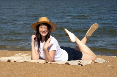 Temiz hava soluyan rahat bir kadının yan görüntüsü, parlak sıcak güneşin altında kumların üzerinde uzanan deniz ve gökyüzü arka planda.