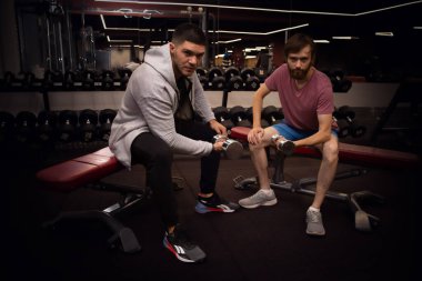 Acemi sporcu ve antrenör halterleri ve spor egzersizleriyle bir bankta otururlar. Yardımcı olmak alıştırmanın doğruluğunu gösterir