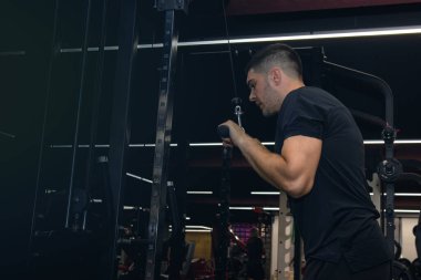 Spor salonunda göğüs ve kablo çaprazlama egzersizleri yapan kaslı bir adam..