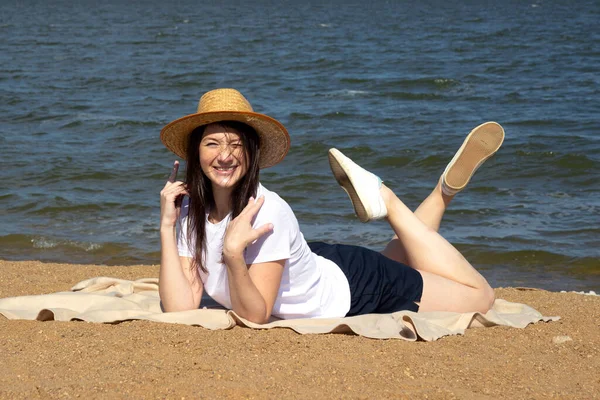 Temiz hava soluyan rahat bir kadının yan görüntüsü, parlak sıcak güneşin altında kumların üzerinde uzanan deniz ve gökyüzü arka planda.