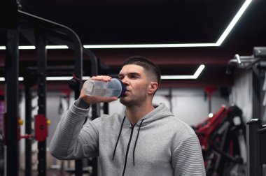 Kaslı adamlar protein ya da su içer, spor salonunda enerji içeceği. Sporcu elinde kopya alanı olan bir titretici tutuyor