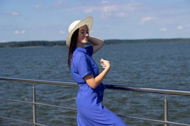 İskelede saman şapkalı, zarif elbiseli genç bir kadın harika bir manzaranın tadını çıkarıyor..