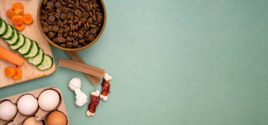 Doğal malzemeli kurutulmuş hayvan maması. Çiğ et, sebze, salatalık ve havuç yeşil arka planda yumurtanın yanında fotokopi alanı ile birlikte. düz yat