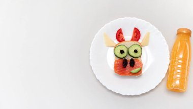 Kızarmış ekmek, kırmızı balık, peynir, sebze üzümü ve meyve suyundan yapılmış yenilebilir 2021 boğa ineği sembollü komik bir sandviç. Çocuklar için kahvaltı fikri. Noel yemeği üst görünümü. kopyalama alanı olan yemek sanatı